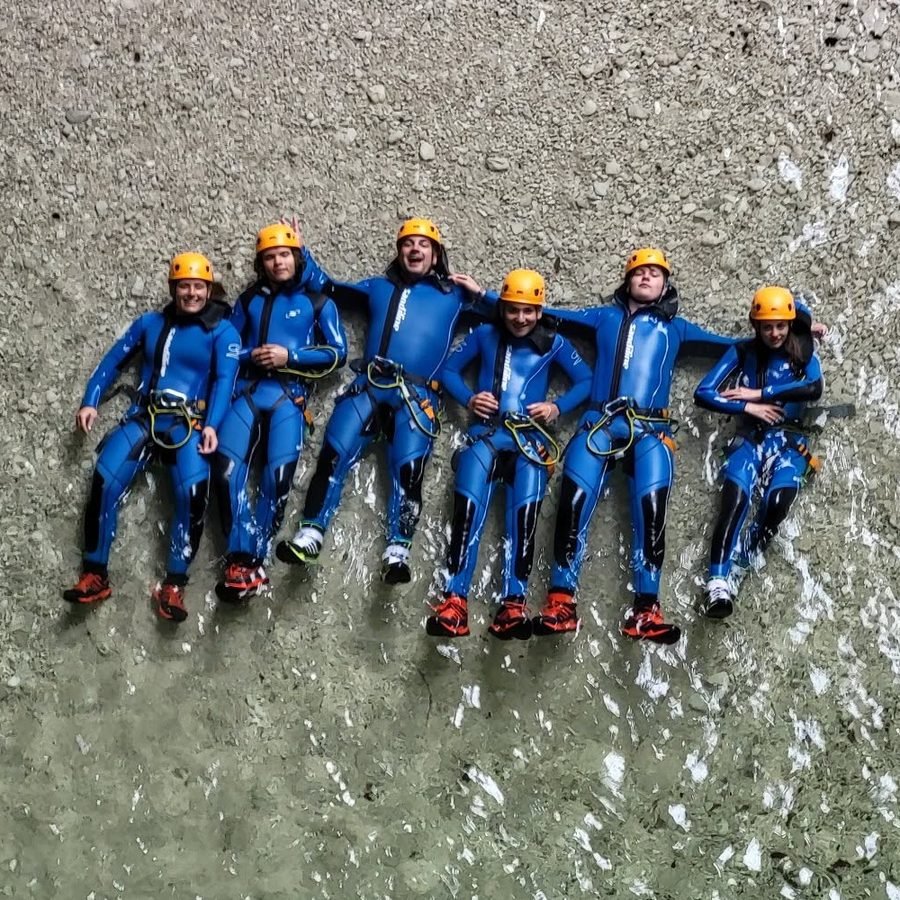 Zes leden liggen lachend op een rij in helder water tijdens een canyoningtocht